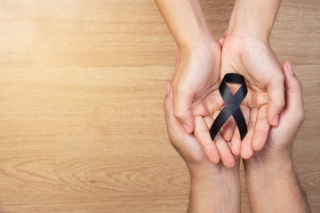 Man hands holding a black ribbon on wooden background