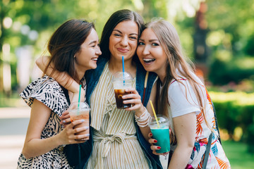 Summer lifestyle portrait multiracial women enjoy nice day, holding glasses of milkshakes. Happy friends in the park on a sunny day. Best friends girls having fun, joy. Lifestyle. Asian, jewess and