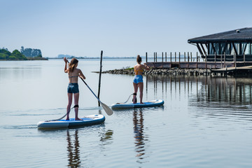 Obraz na płótnie Canvas Two women stand up paddleboarding