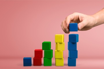 Hand with toy wooden blocks stack, towers of blank multicolor