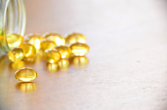 Fish oil capsules on wooden background, vitamin D supplement, selective focus, copy space for text.