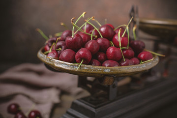 Freshly Picked Cherries in an Antique Scale on Warm Brown Background