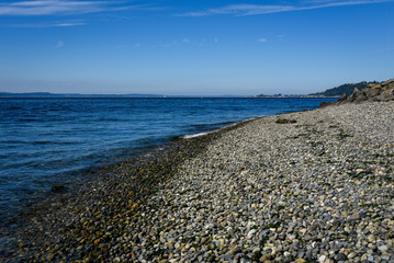 Fototapeta na wymiar Rocky Puget Sound beach landscape, small rocks, calm sea with small waves, distant island and blue sky with clouds 