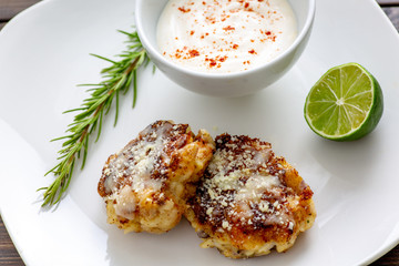Two shrimp cakes on a white plate with a lemon garlic dipping sauces lemon wedge and a stem or rosemary on a wooden table.