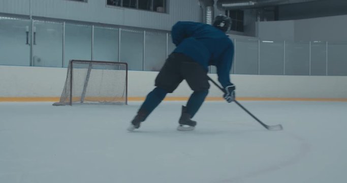 Caucasian male ice hockey player practicing slap shot at the training arena alone, misses the net. 4K UHD 60 FPS