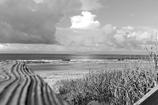 Fototapeta Wooden boardwalk path through the sand dunes to the Atlantic Ocean beach, Sunset Beach, North Carolina, in black and white
