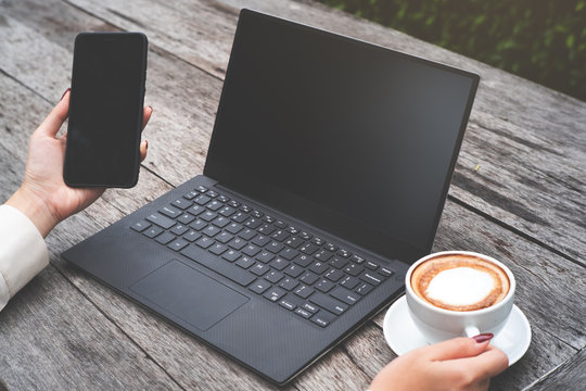 Mock up image of  woman hold smart phone and laptop on wood table, and one hand hold coffee cup.