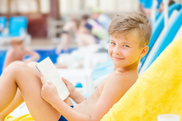 Little boy reading a book by the pool.  Relaxation resting vacations concept