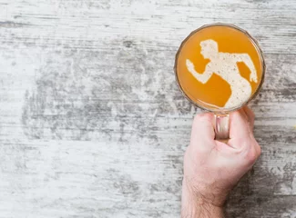 Foto auf Leinwand man's hand holds a mug of beer with a silhouette of a running man. Top view. Space for text © Ermolaev Alexandr