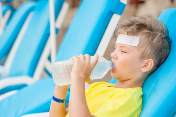 Little boy on the beach with a sunstroke drink water
