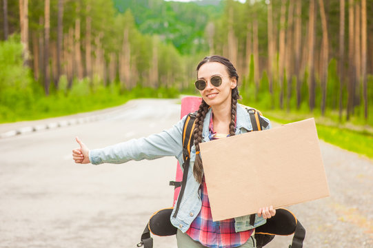 Smiling girl travels hitchhiking with a cardboard sign in her hands. Space for text