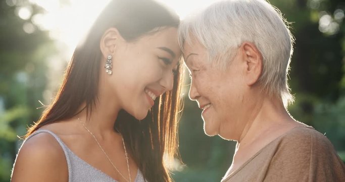Happy asian grandmother and her teen granddaughter standing in park, hugging each other and smiling - portrait shot 4k