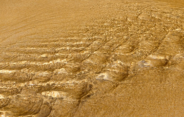 Golden sand under transparent sea water, abstraction, texture, background  of sand pattern on a beach in the summer closeup of sand under the water