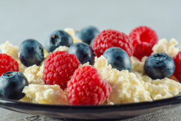 Cottage cheese with fresh raspberries and blueberries in a plate for a healthy breakfast with ripe berries. A natural healthy product.