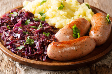 Full lunch of mashed potatoes with stewed red cabbage and fried sausages close-up on a plate....