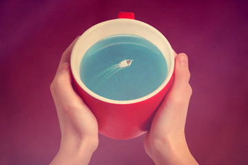 Red cup of coffee with the boat and the sea inside. Creative idea