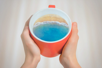 Red cup of coffee with the sea and the beach inside. Creative idea