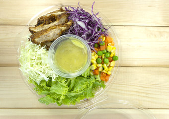 Chicken Salad in Plastic Box on wooden floor, props decoration with Green salad, cauliflower purple, beans, peas, carrot and sausage in a cup,Top view.