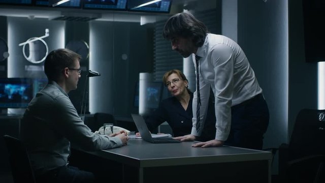 Male and Female Special Service Agents Interrogate Young Suspect in Cyber Crimes, Officer Looses Temper and Threatens Accused while Questioning. Dark Interrogation Room.
