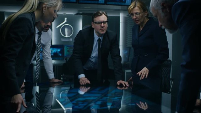 Diverse Team of Government Intelligence Agents Standing Around Digital Touch Screen Table and Tracking Suspect. FBI Agents Using Satellite Surveillance in the Dark Monitoring Room.