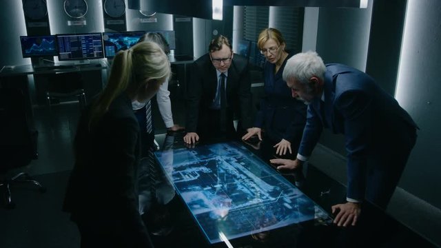 Team of Government Intelligence / FBI Agents Standing Around Digital Touch Screen Table and Tracking Suspect Vehicle Using Satellite Surveillance in the Monitoring Room.