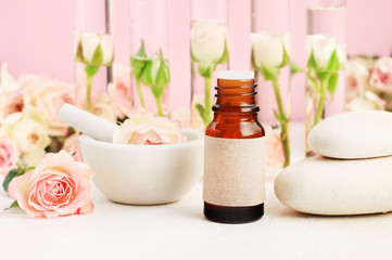 Aromatherapy spa set delicate light pink background with Essential oil bottle, stones, roses. Herbal extract product natural skincare. 