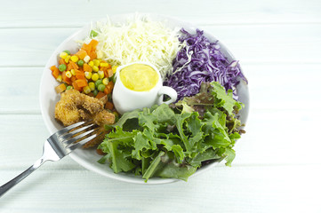 Healthy salad diet food concept, props decoration tomatoes, lemon, Green pepper, avocado, green and Purple Salad in Glass Plate on wood floor background, Top view with copy space for your text..