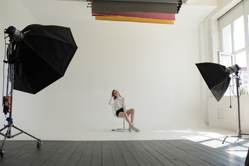 Model is sitting and posing in a professional photo studio on a white background.