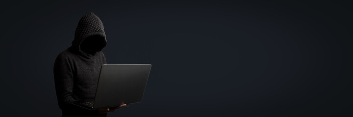 Faceless man in a hoodie with a hood holds a laptop in his hands