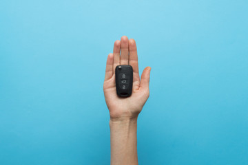 Female hand holds a car key in the palm on a blue background. Co