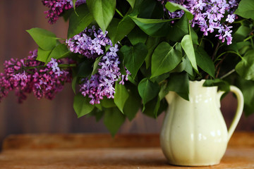 Home interior decor, bouquet of lilacs in a vase and books on rustic wooden table, on a white wall background