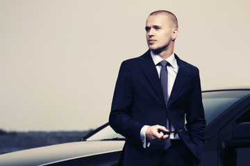 Young businessman in dark blue suit next to his car