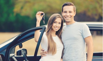Young happy couple standing by car smiling - concept of buying