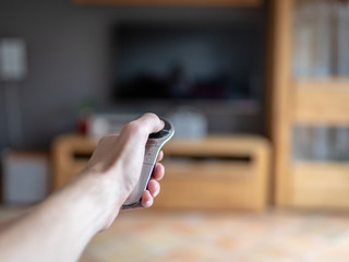 Eine männliche Hand hält eine moderne Fernbedienung und zeigt damit auf den Fernseher