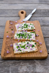 Dairy and lactose-free vegan cream cheese spread made from cashew and macadamia nuts on crackers with knife, fresh chopped chives and edible chive flowers with shallow depth of field