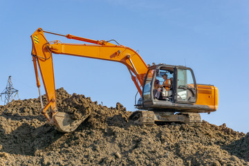 Orange excavator loads the land on a construction site..