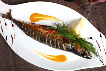 Grilled fish on white plate with herbs and lemon on wooden background, top view. Mediterranean luxurious seafood concept.