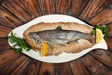 Grilled fish on white plate with herbs and lemon on wooden background, top view