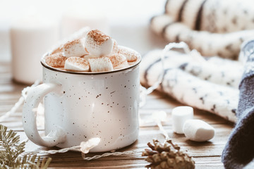 Hot cocoa with marshmallow in a white ceramic mug surrounded by winter things on a wooden table....