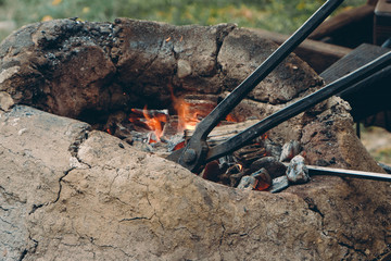 Close up of medieval furnace with iron tongs, burning coals and fire in blacksmith forge
