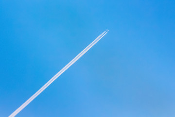 An airplane and a trail from an airplane in a blue sky