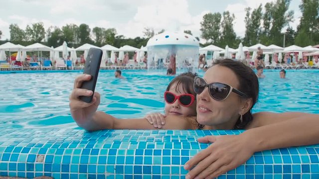 Happy family in the pool. A woman with a child is making a selfie in a bassin. Mother and daughter are photographed in the water park.