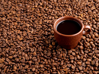 brown cup of espresso on background of scattered coffee beans, side view, copy space