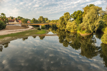 Fototapeta na wymiar Holzbrücke mit teilweise bewölktem Himmel spiegelt sich in Fluss