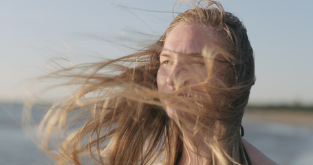 closeup portrait of young girl standing on a beach and wind blows her hair