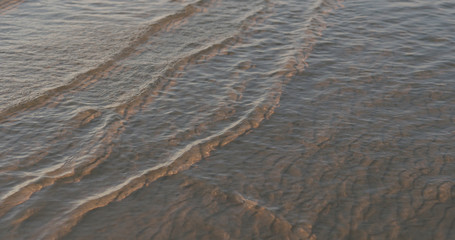 closeup of small waves with caustics on a beach at sunset