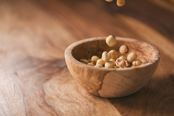 peeled hazelnuts falling in wood bowl with copy space