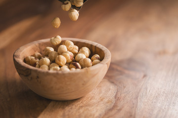 peeled hazelnuts falling in wood bowl with copy space