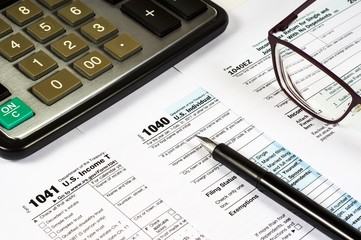 Tax Form 1040, 1041, 1040EZ and pen on a background of a calculator and glasses, close-up