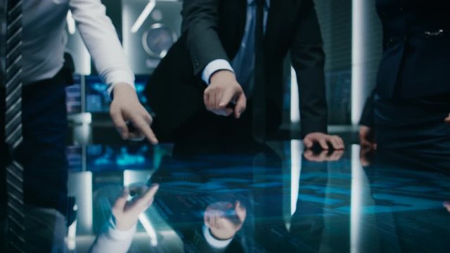 Diverse Team of Government Intelligence Agents Standing Around Digital Touch Screen Table and Satellite Tracking Suspect, Pointing at Display. Big Dark Surveillance Room. 